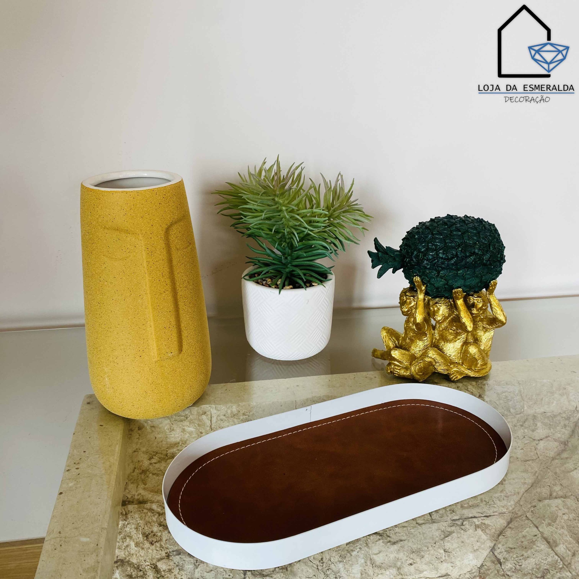 Vaso amarelo, planta artificial em vaso branco, escultura dourada com folhas verdes em superfície de mármore com tabuleiro