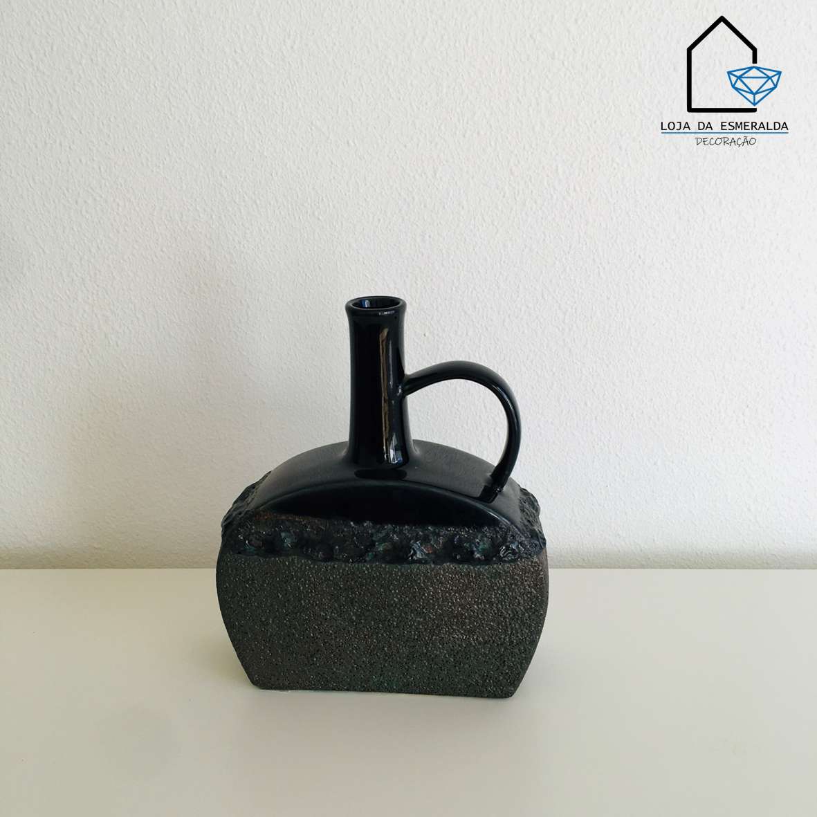 Vaso quadrado cinza e preto com alça e gargalo fino sobre superfície branca