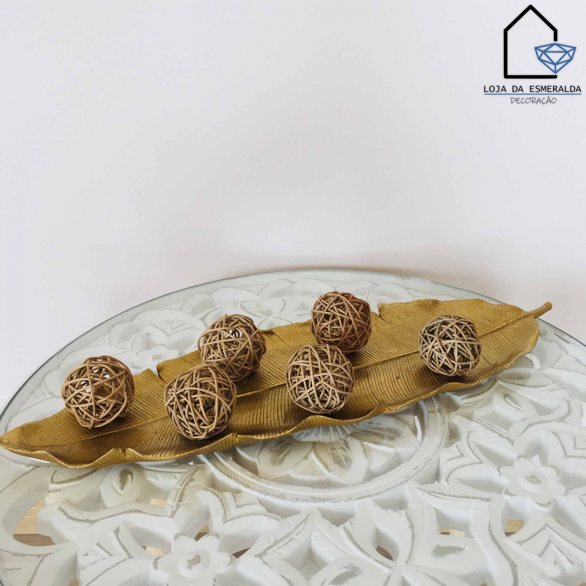 Conjunto decorativo dourado com bolas de rattan sobre mesa branca decorada.