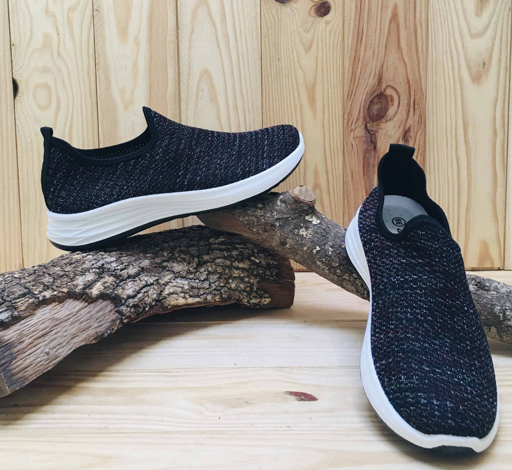 Par de sapatilhas pretas tricotadas com sola branca em suporte de madeira