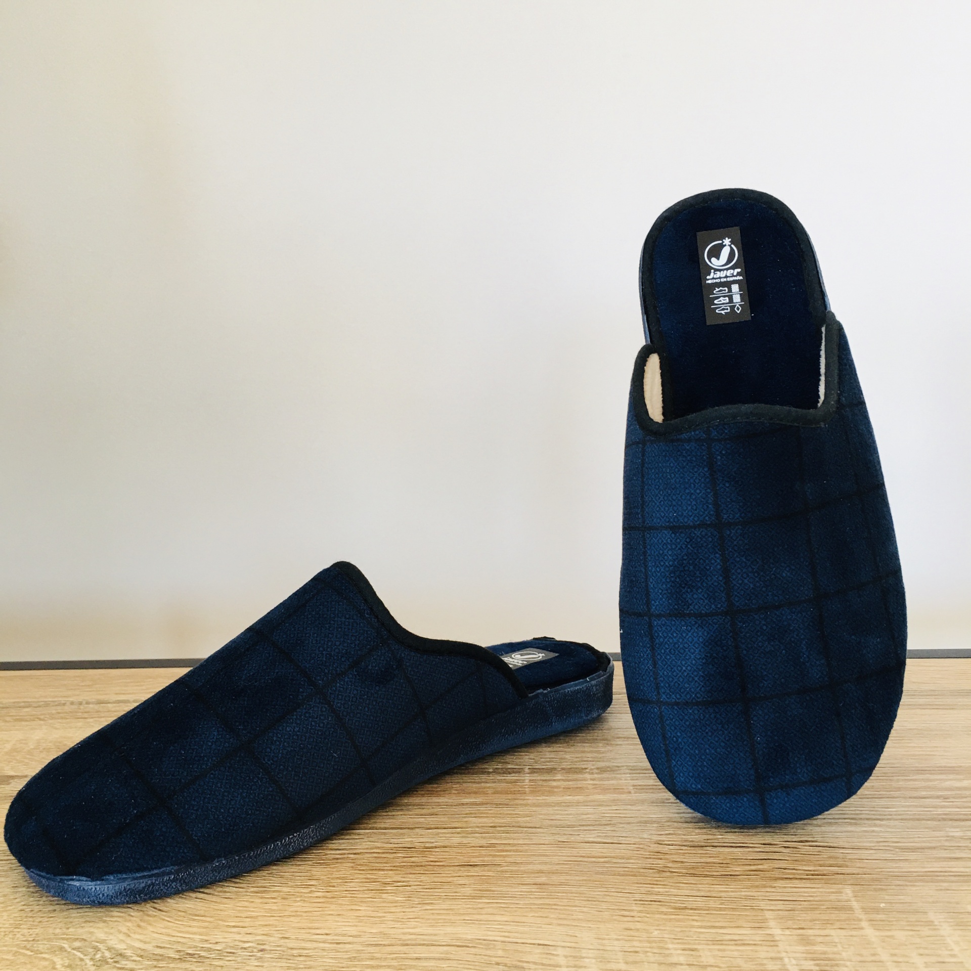 Chinelos de casa azul escuro com padrão quadriculado sobre superfície de madeira.