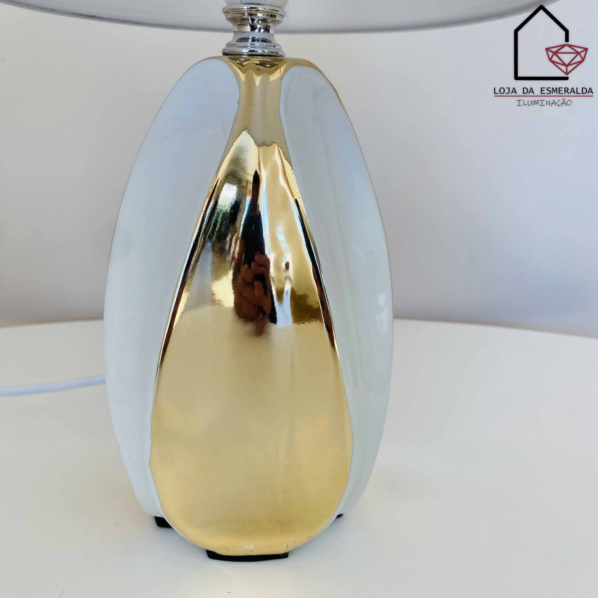 Candeeiro de mesa dourado e branco com logótipo Loja da Esmeralda ao fundo
