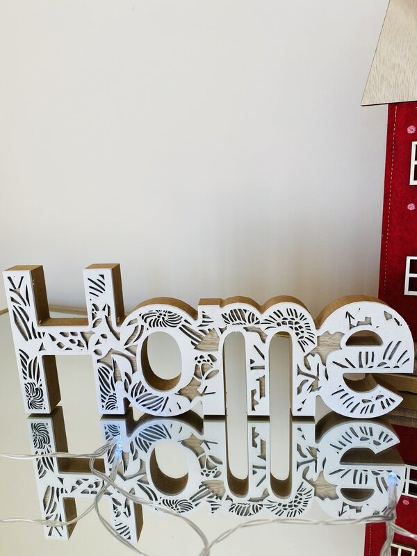 Letreiro decorativo branco em madeira com padrão floral na palavra 'Home' sobre superfície espelhada