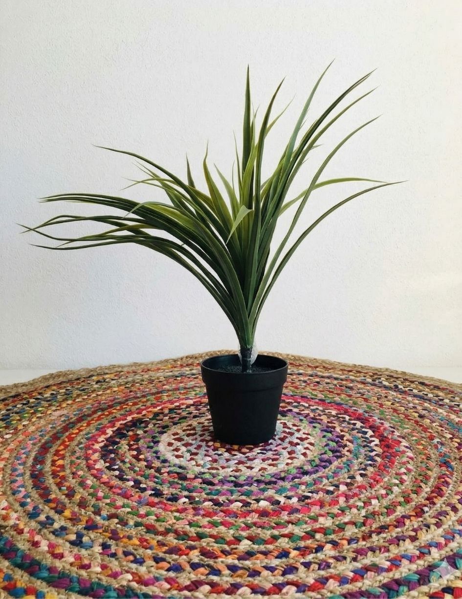 Planta artificial em vaso preto sobre tapete redondo colorido