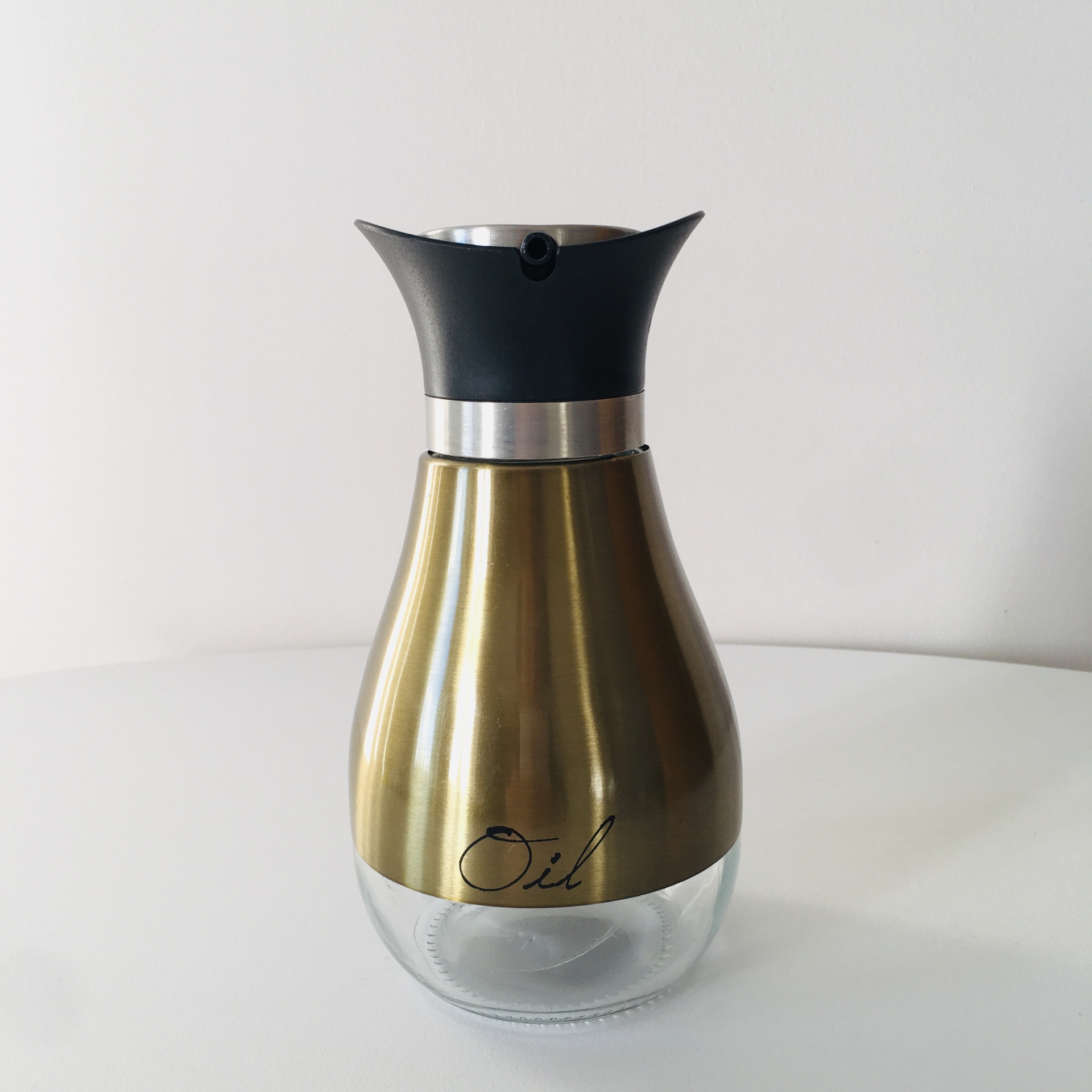 Garrafa doseadora para óleo dourada com tampa preta sobre mesa branca