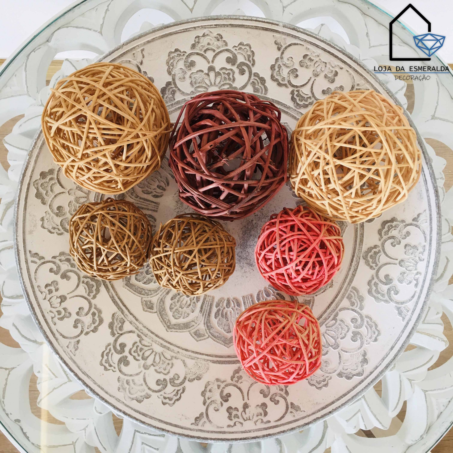 Bolas decorativas de rattan coloridas num prato branco com desenho ornamental cinzento