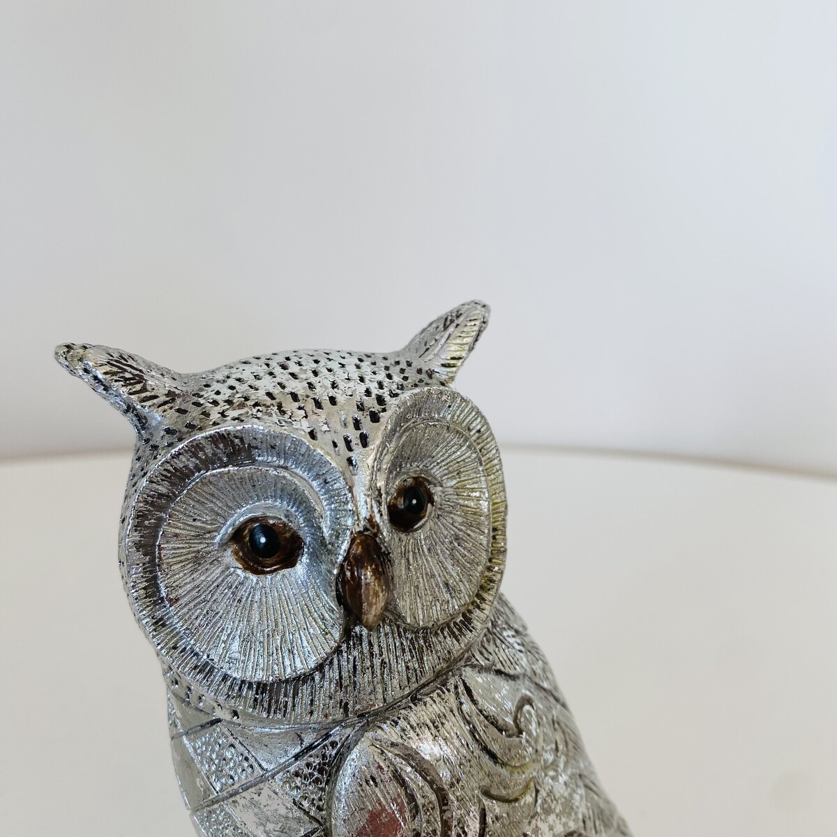 Figura decorativa de coruja em metal prateado com olhos castanhos