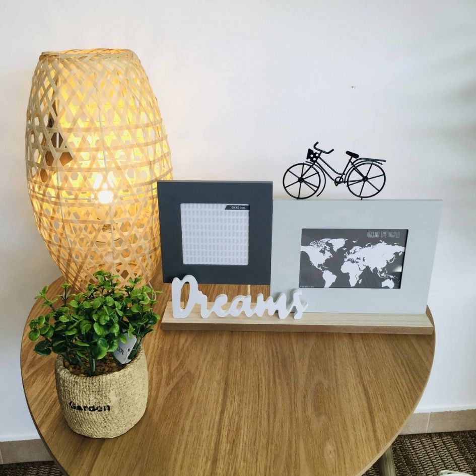 Mesa com lâmpada, planta, molduras de fotos e decoração com palavra Dreams
