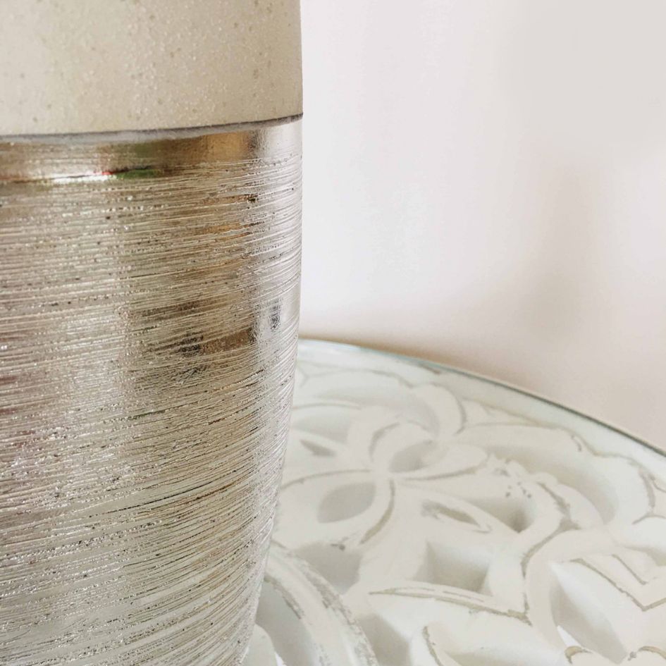 Vaso prateado e cerâmico sobre superfície de vidro com padrão branco em relevo