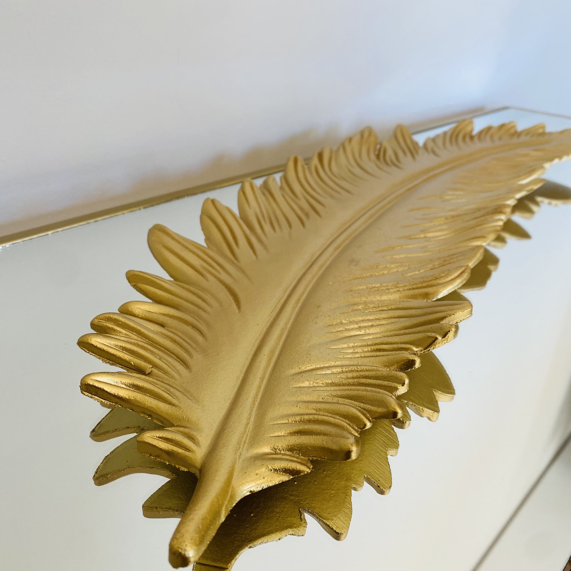 Prato decorativo dourado em forma de folha sobre superfície espelhada