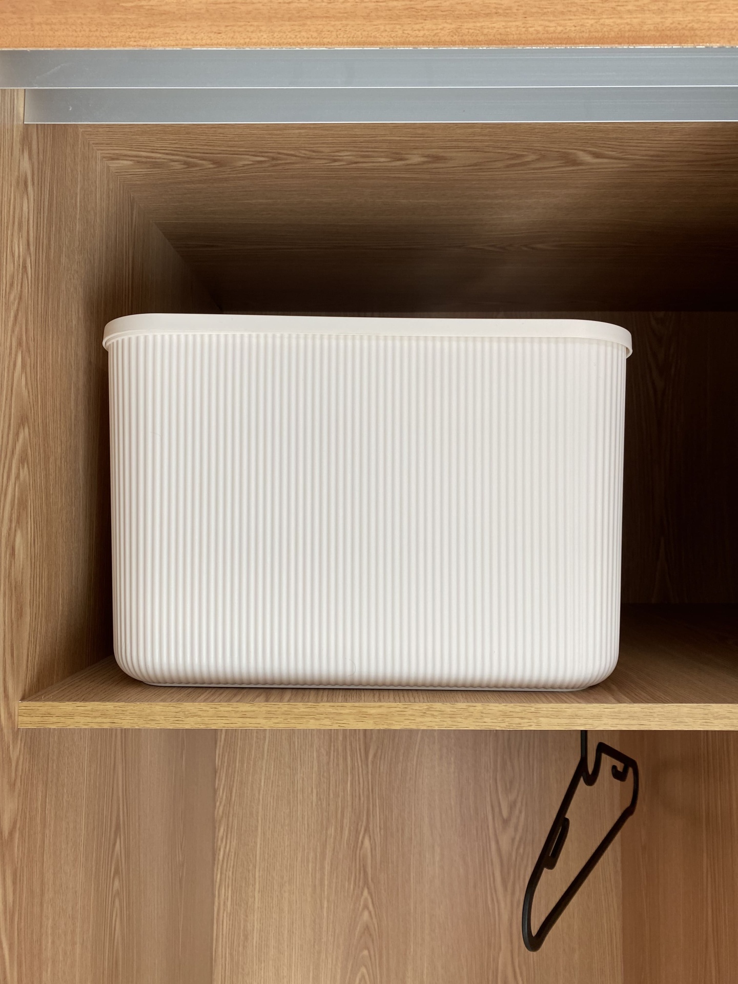 Contentor branco canelado numa prateleira de madeira clara com cabide preto pendurado abaixo.