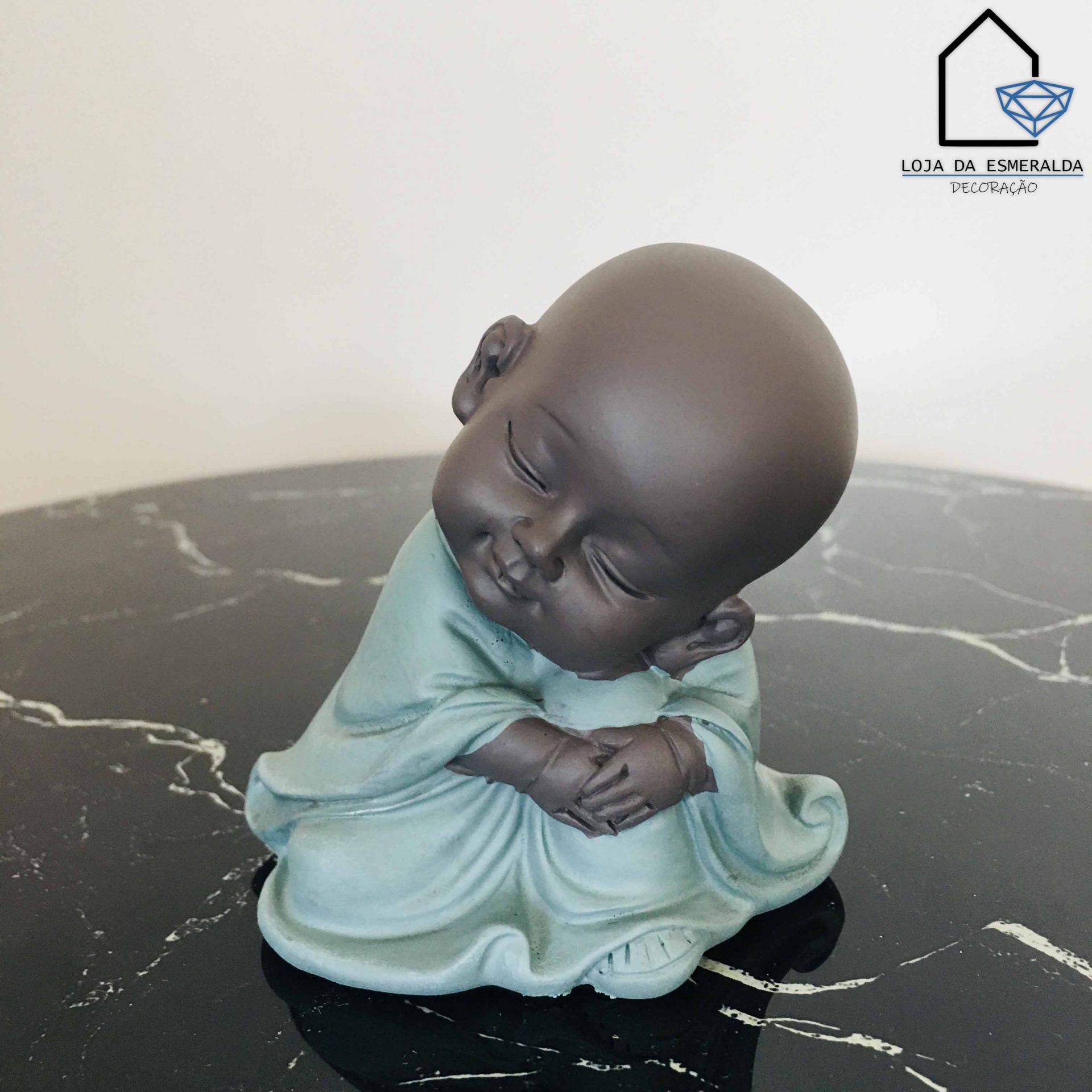 Estátua de bebé monge sentada com roupa azul sobre superfície preta