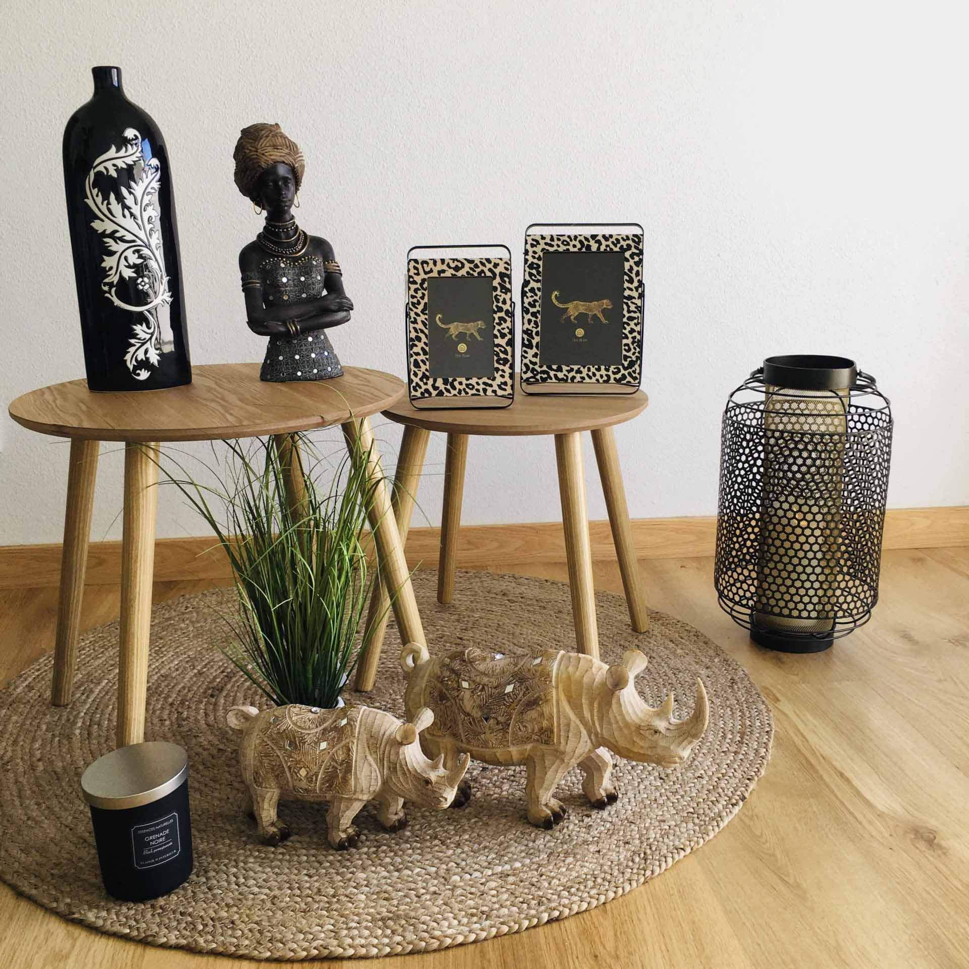 Conjunto decorativo com mesas de madeira, vasos, molduras com escorpião, esculturas de rinocerontes, vela preta e candeeiro metálico num tapete de fibras naturais.