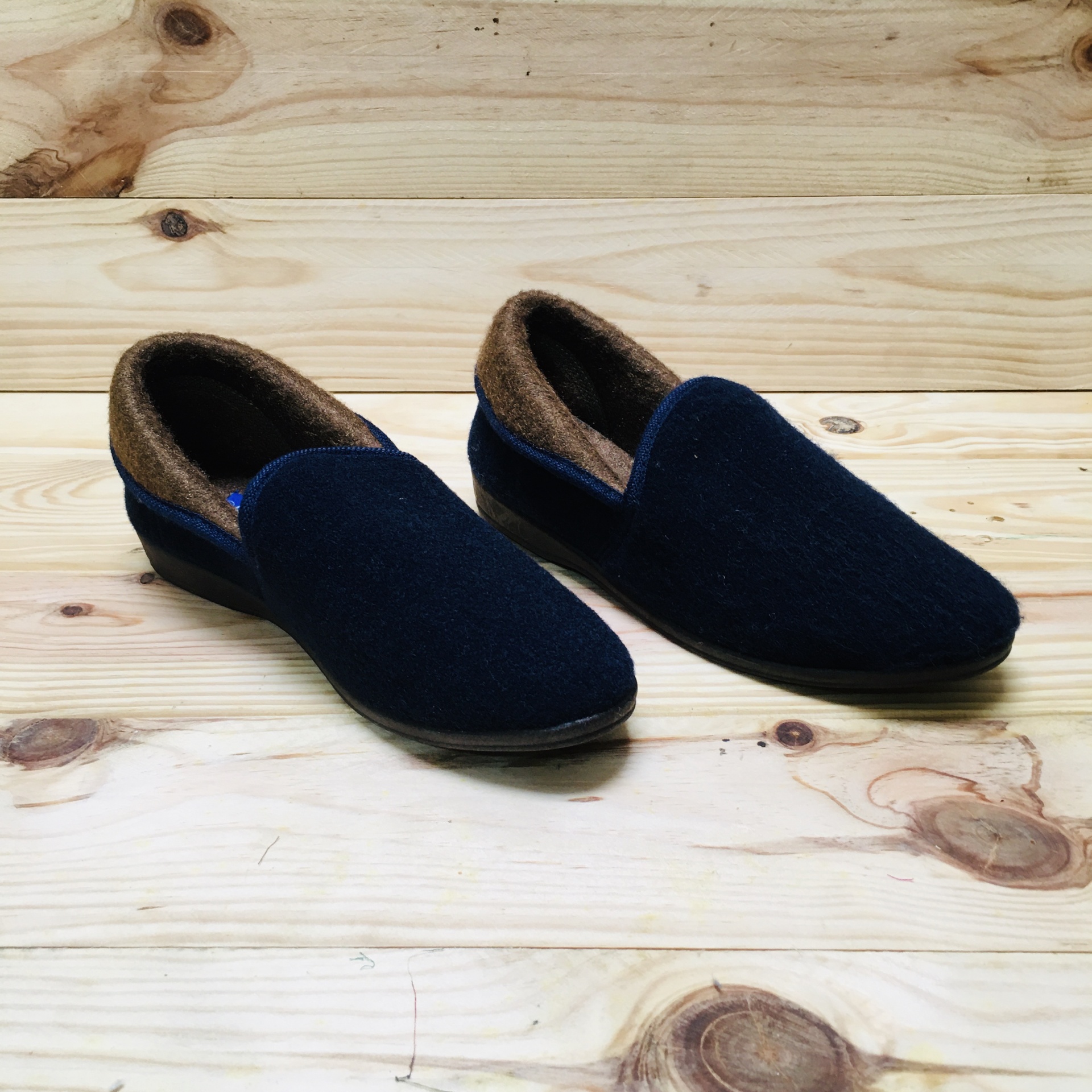Chinelos ou mocassins azul escuro com interior castanho e solado preto sobre madeira clara
