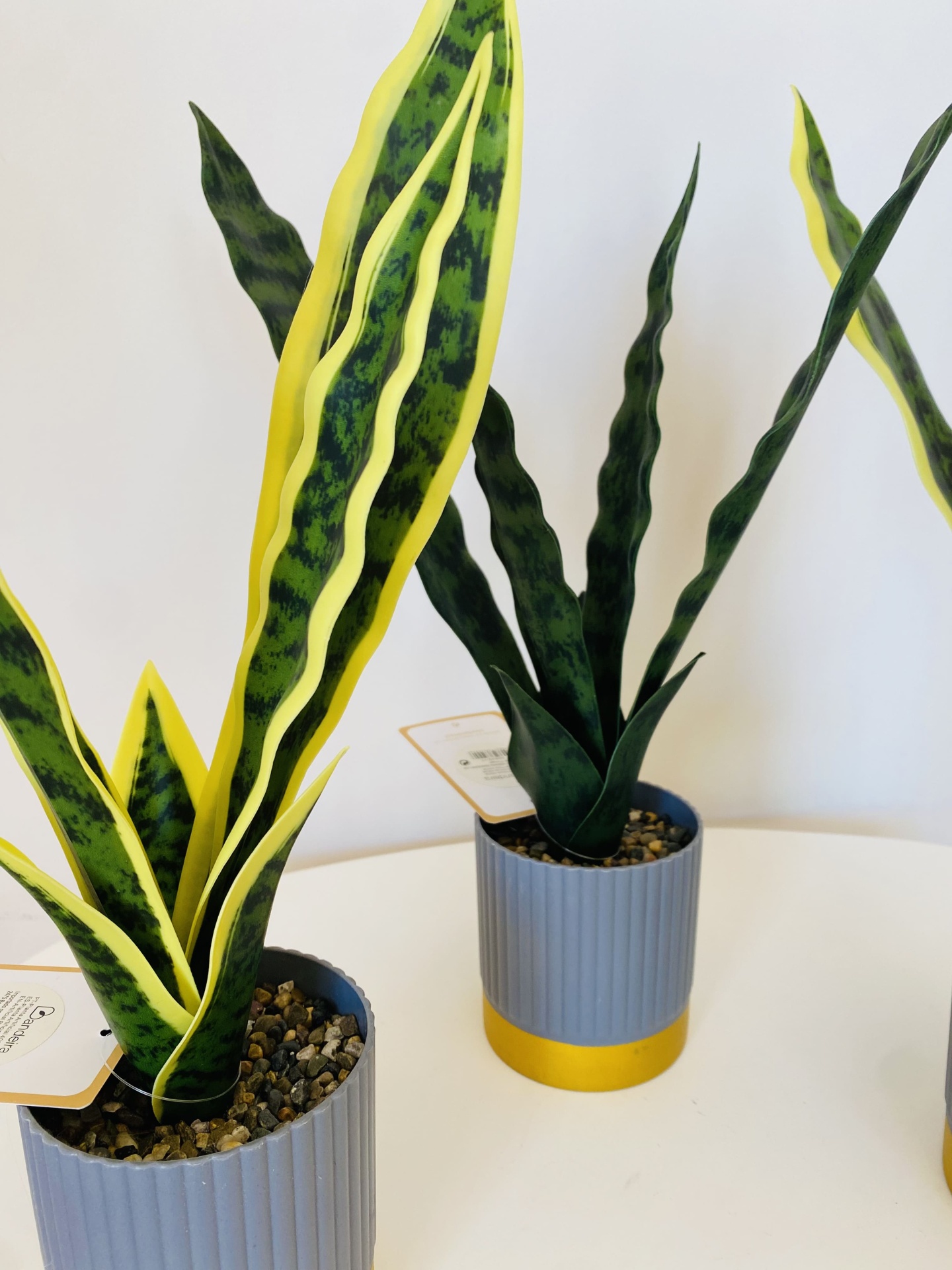 Três vasos cinzentos com plantas artificiais de folhas verdes e amarelas em fundo branco
