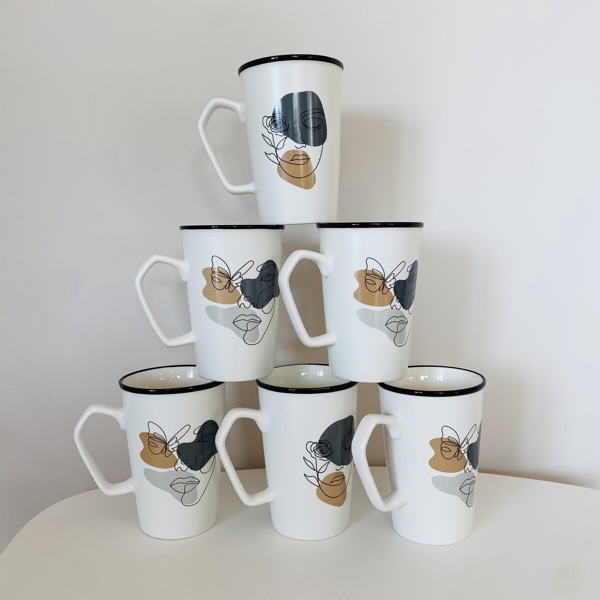 Seis canecas brancas com padrão abstrato preto e bege empilhadas em pirâmide