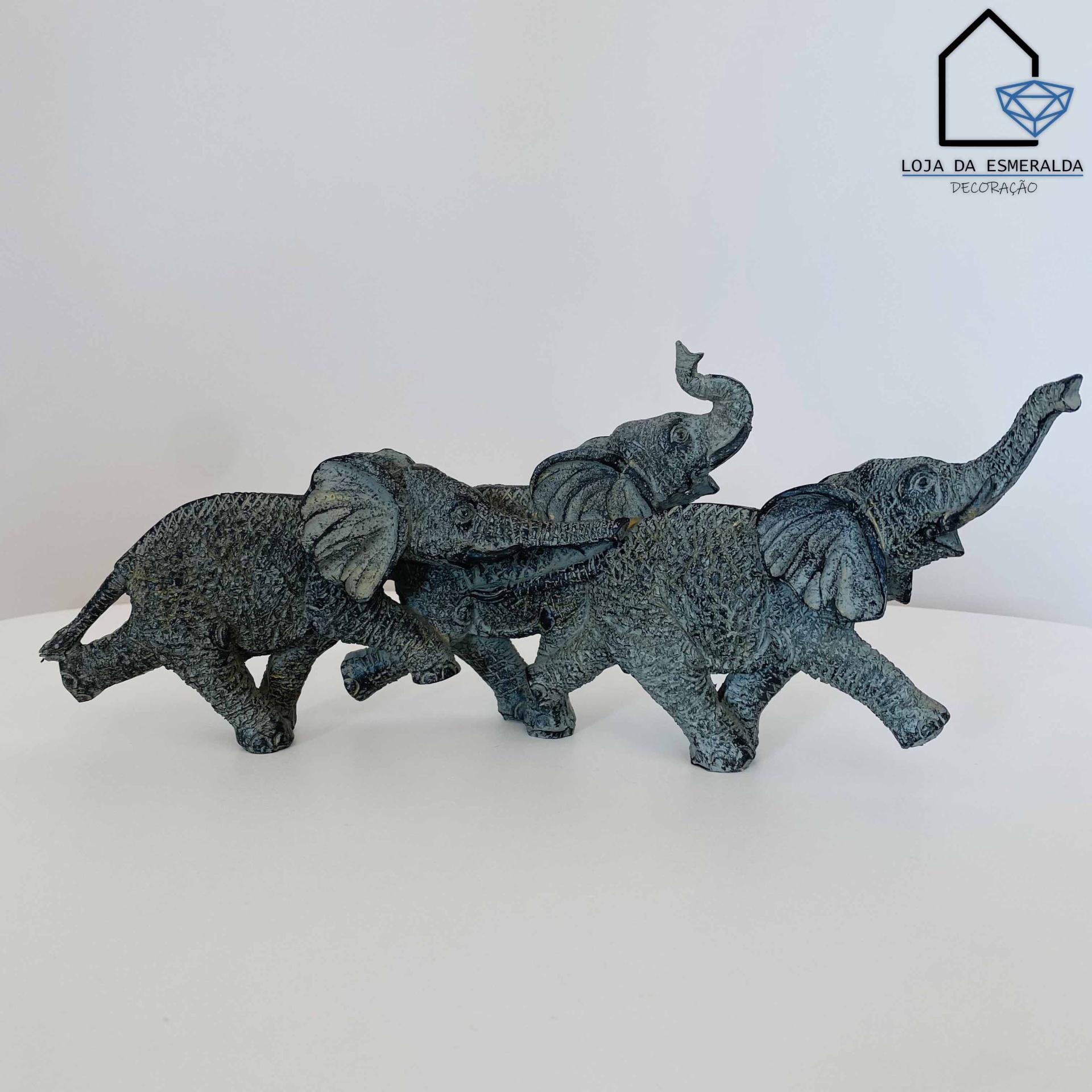 Três esculturas cinzentas de elefantes em superfície branca com logótipo de loja no fundo