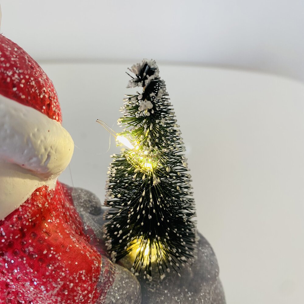 Pai Natal em vermelho com pequena árvore de Natal iluminada