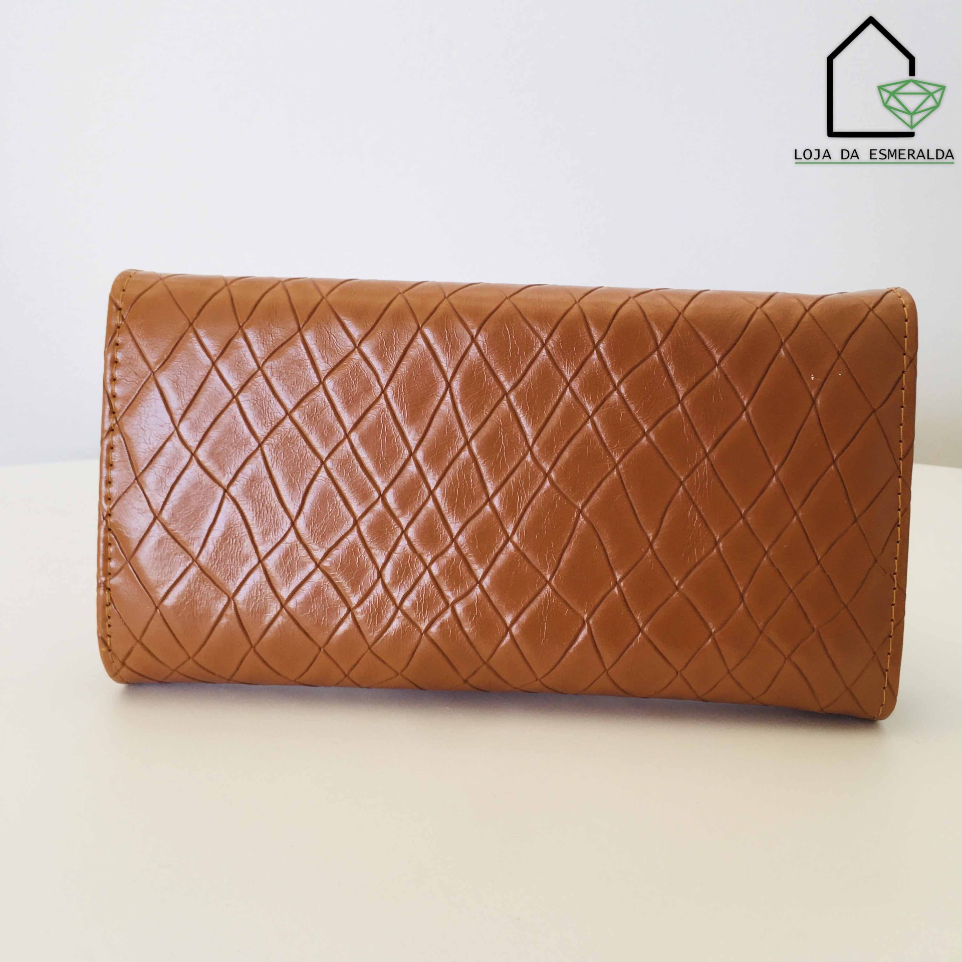 Carteira castanha em pele sintética com padrão em losangos sobre mesa branca