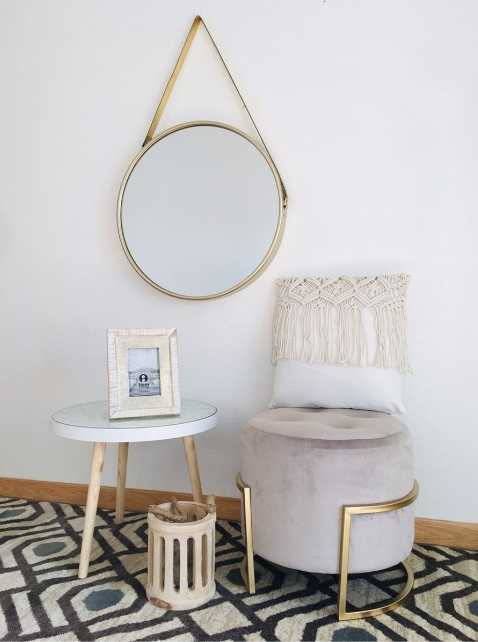 Espelho redondo com moldura dourada e decoração de sala com mesa, puff e almofada