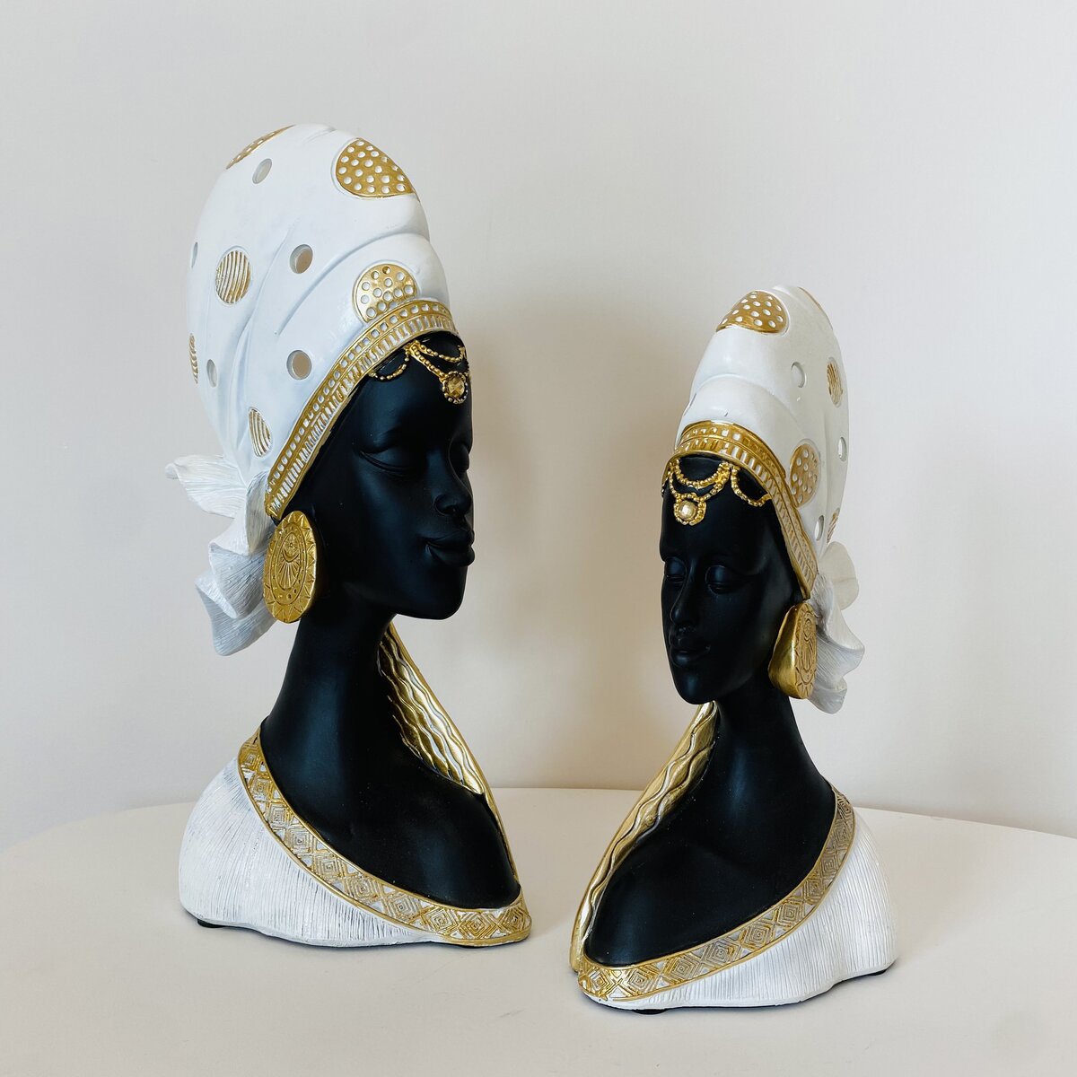 Duas esculturas de bustos femininos com turbantes brancos e detalhes dourados em fundo branco