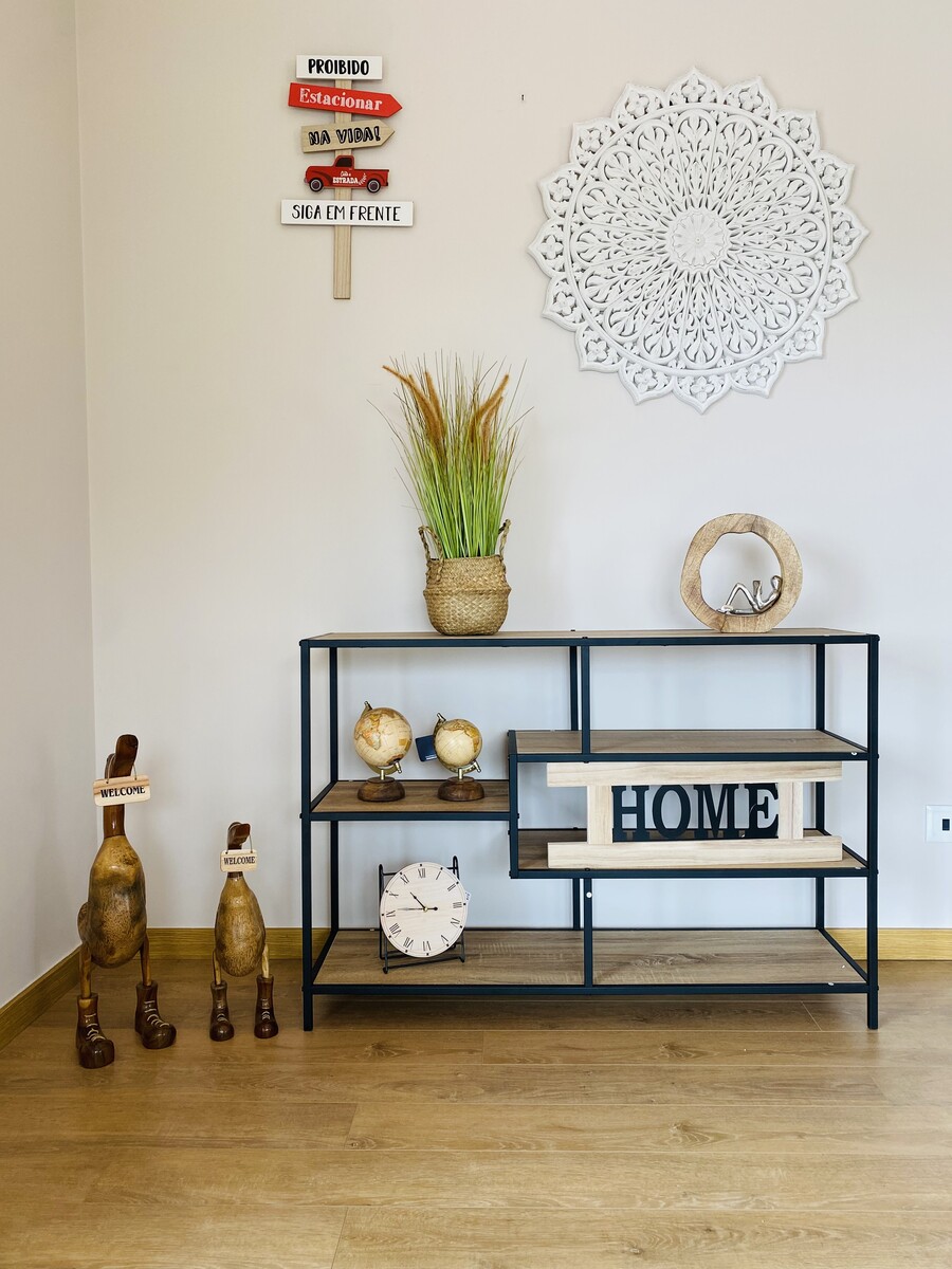 Móvel decorativo em metal preto e madeira clara com vários objetos decorativos e parede branca com decoração