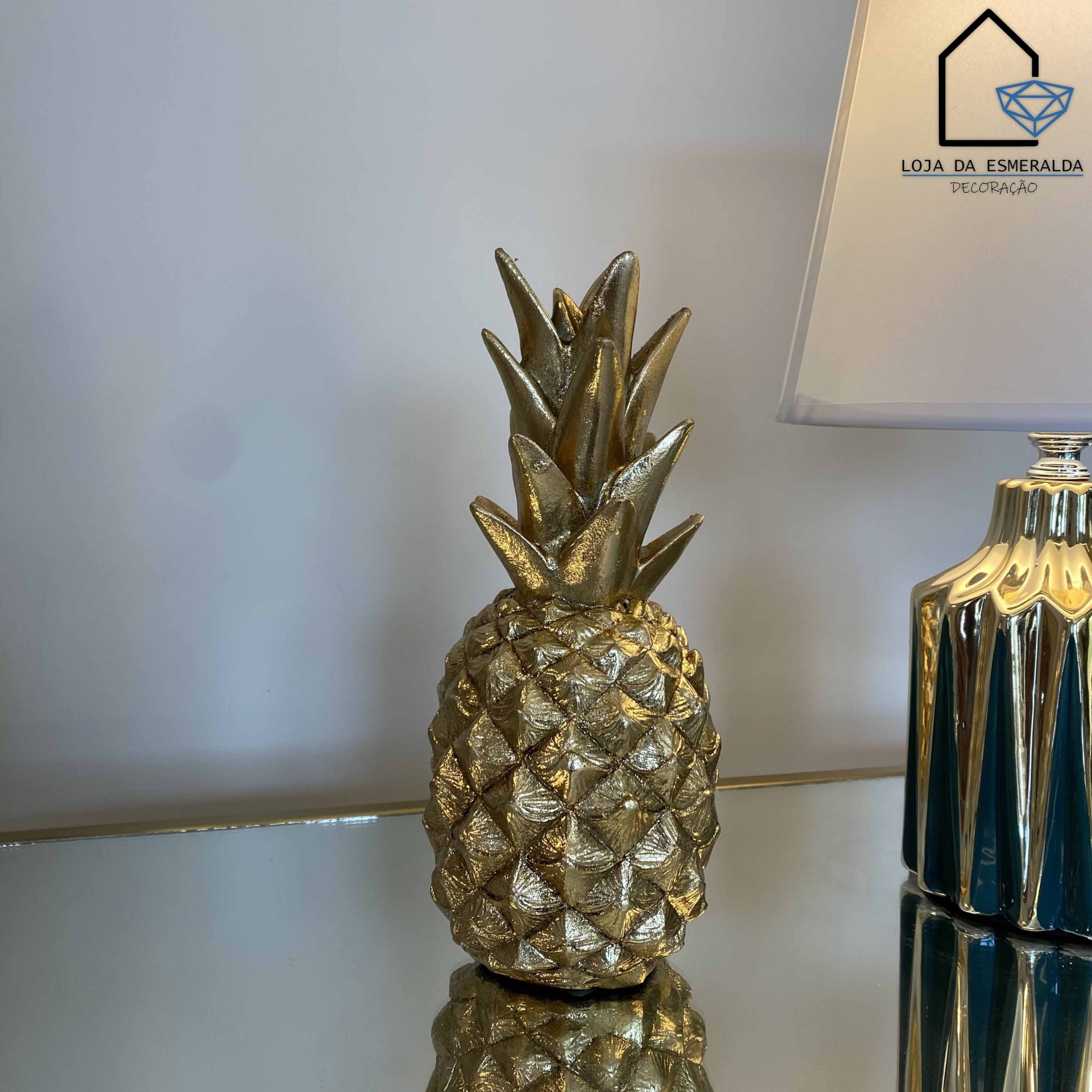 Figura decorativa dourada em forma de ananás numa mesa ao lado de um candeeiro dourado e branco