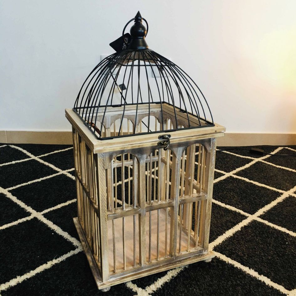 Gaiola decorativa de madeira e metal sobre tapete preto com linhas brancas