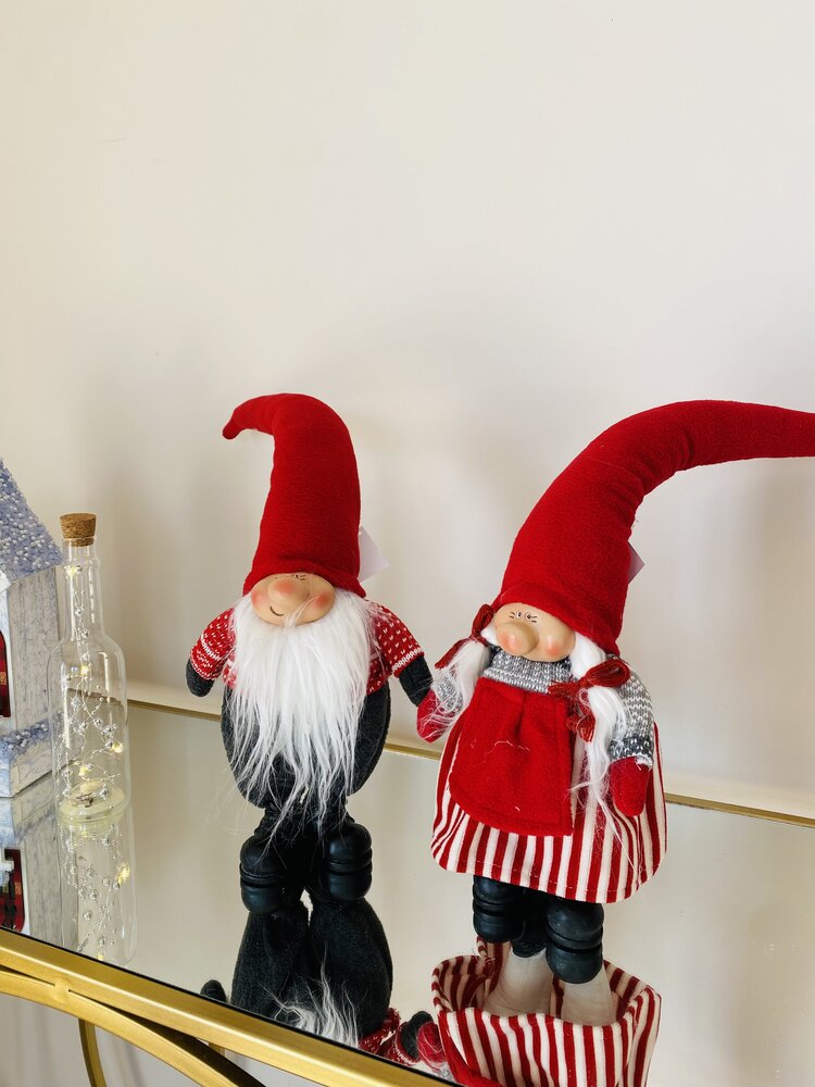 Bonecos decorativos de Natal com gorros vermelhos e roupas vermelhas e brancas sobre superfície espelhada.