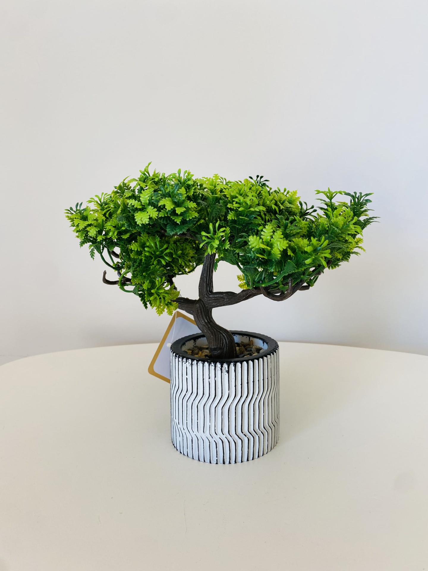 Pequena árvore artificial num vaso decorativo branco com padrão geométrico.
