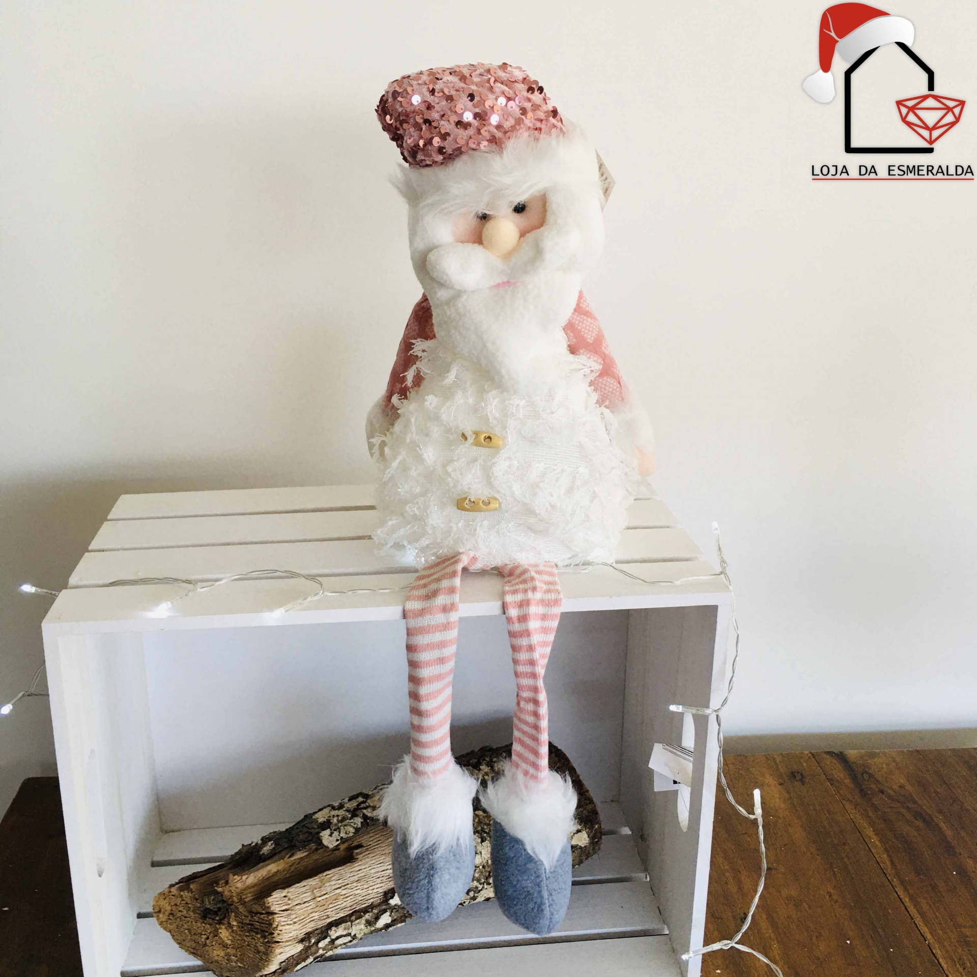 Boneco decorativo de Natal com fato rosa e branco sentado numa caixa de madeira branca