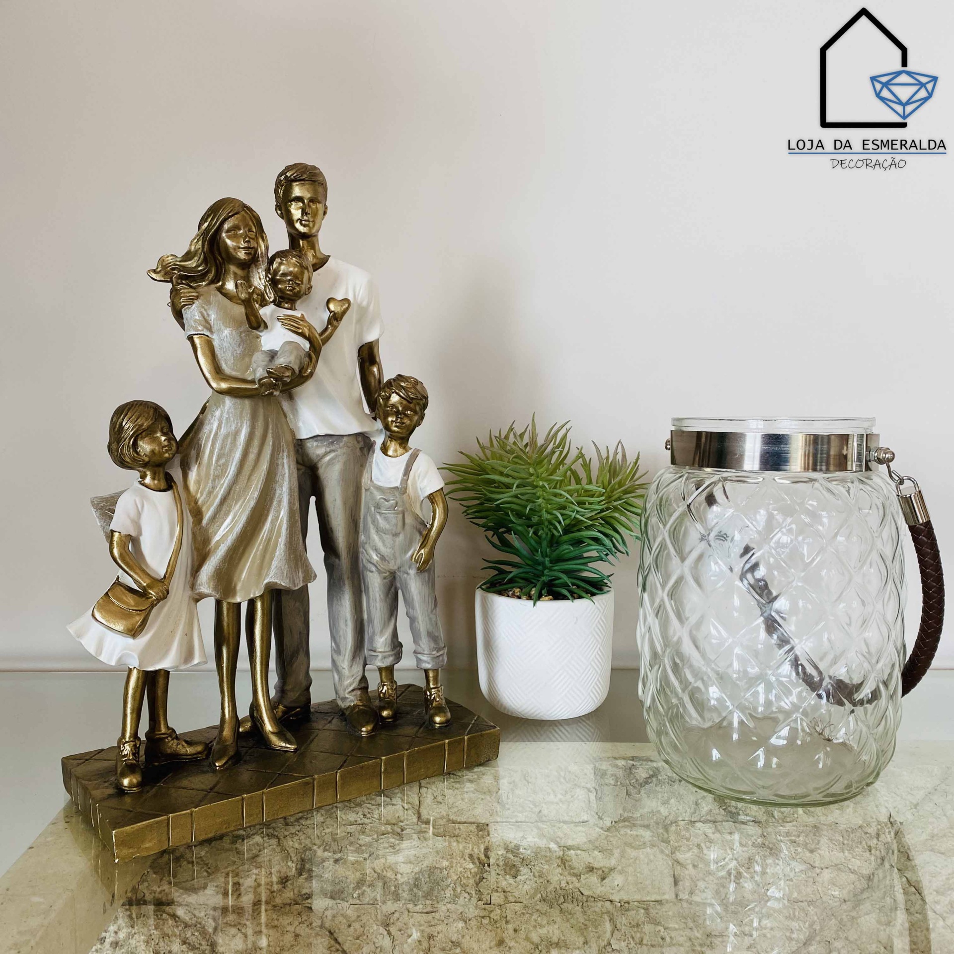 Estátua de família dourada, vaso com planta e jarra de vidro sobre superfície de pedra