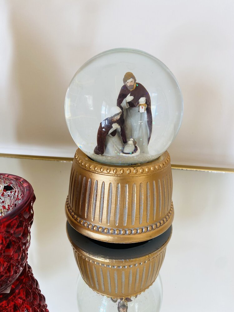 Globo de neve com presépio e base dourada ao lado de objeto vermelho