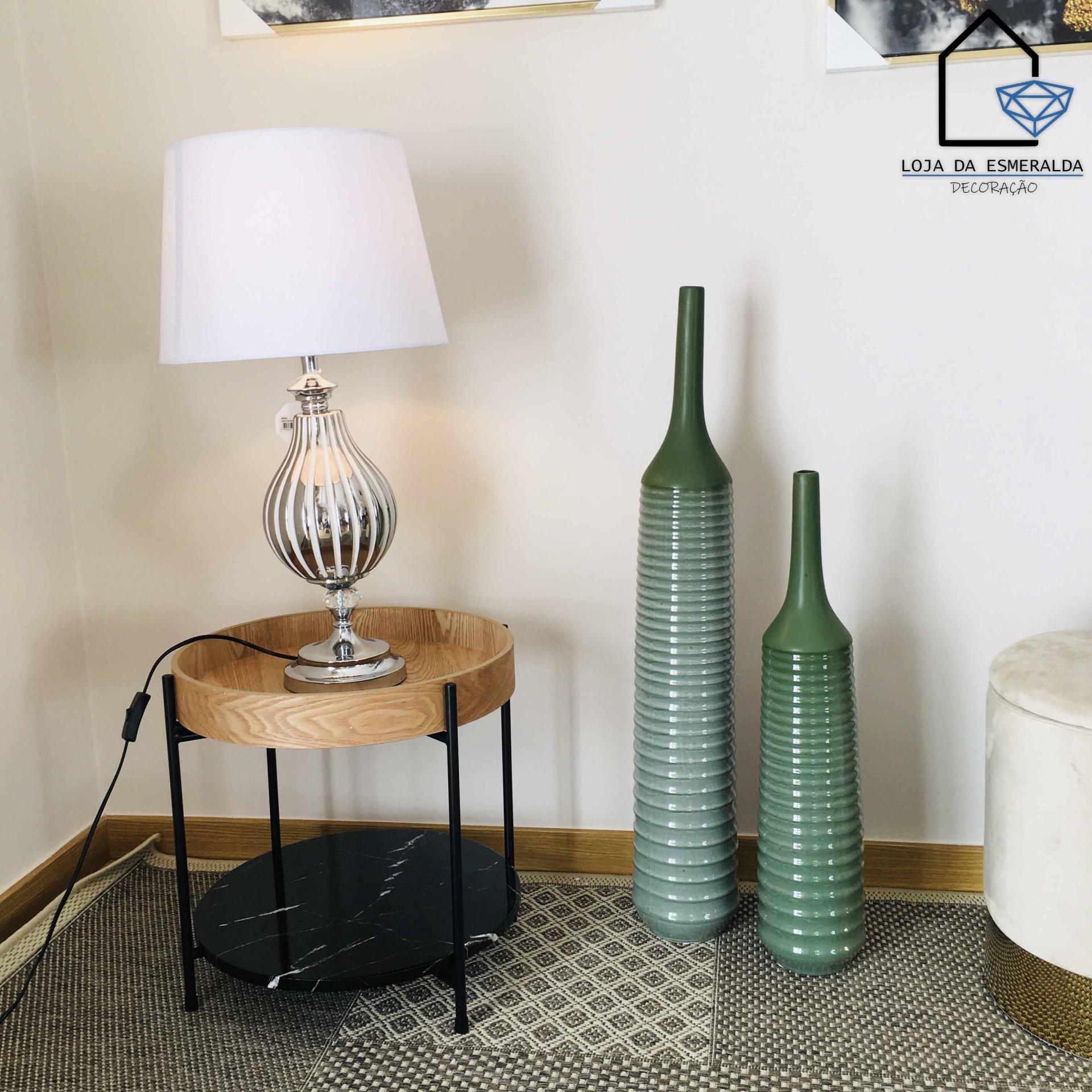 Mesa de apoio com lâmpada e garrafas decorativas verdes junto a puff creme