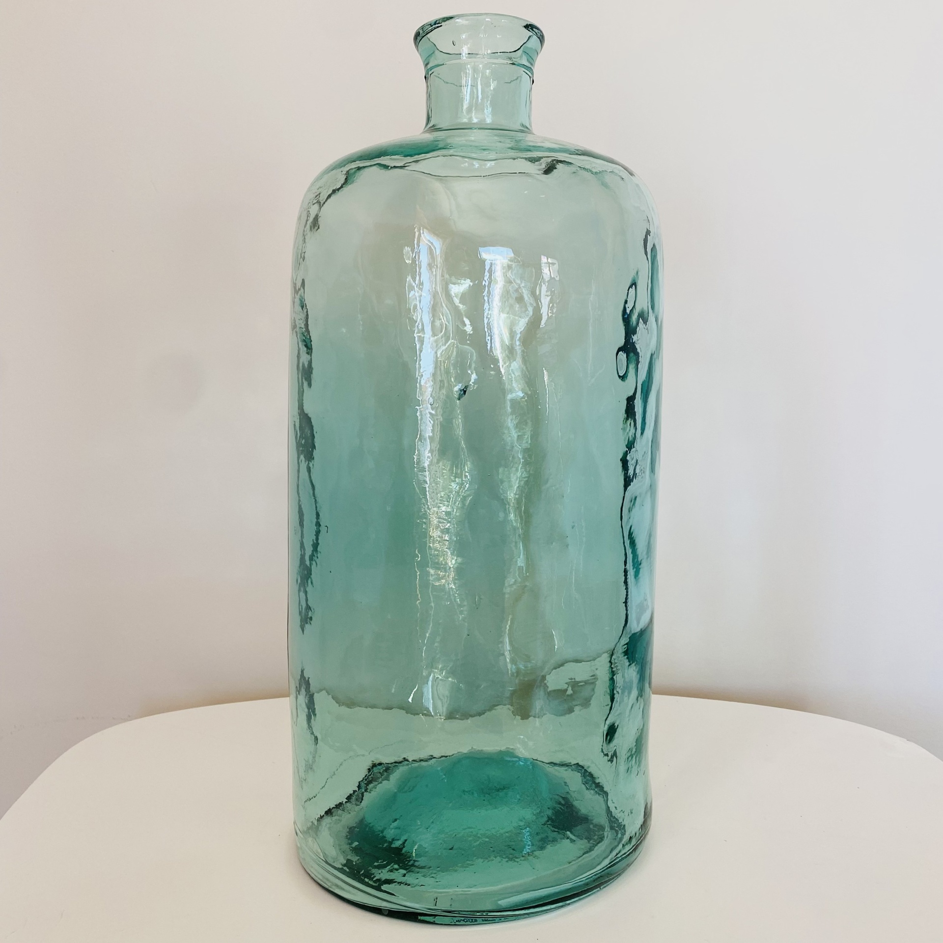 Frasco grande de vidro azul esverdeado com superfície irregular sobre mesa branca