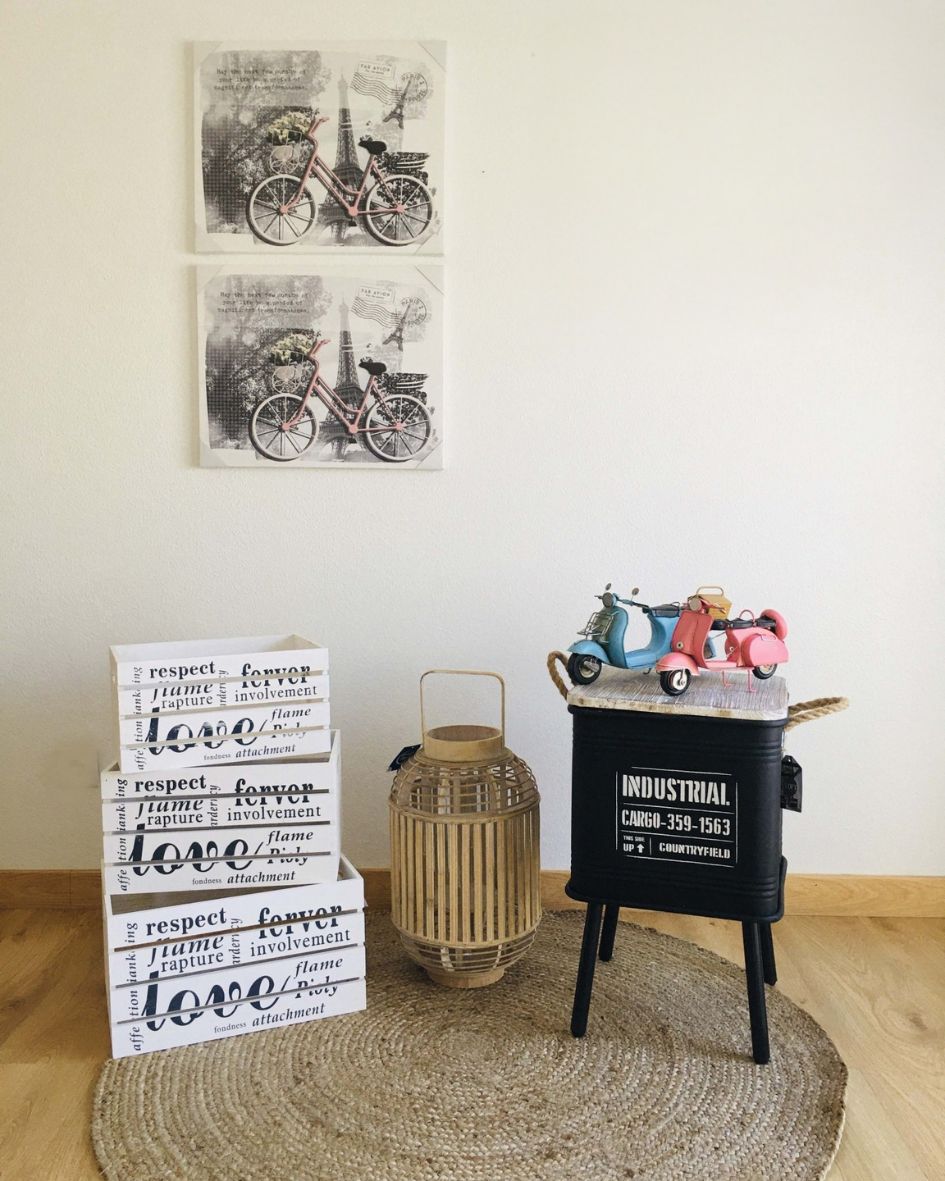 Quatro caixas de madeira brancas empilhadas, candeeiro de madeira, tamborete preto e miniaturas de motos em tapete redondo