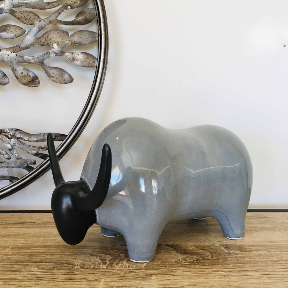 Estátua decorativa de búfalo cinza com cabeça preta e chifres em superfície de madeira