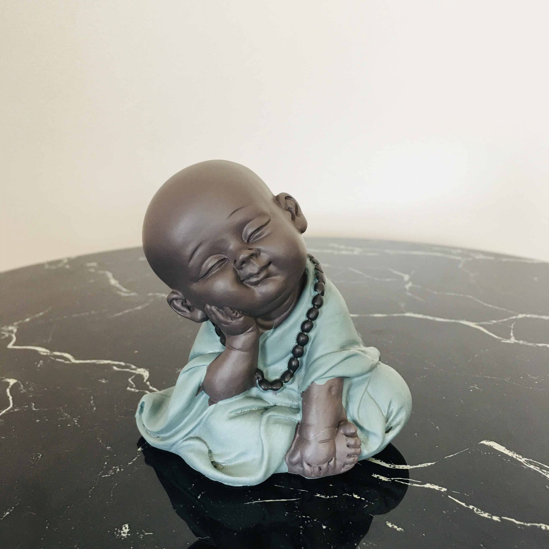 Estátua decorativa de monge bebé em bata azul e colar negro sobre superfície mármore preta