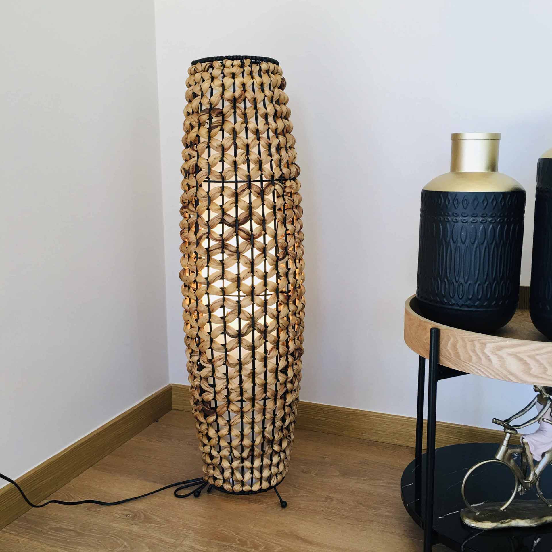 Lâmpada de pé com cordas bege e estrutura preta ao lado de mesa com vasos decorativos
