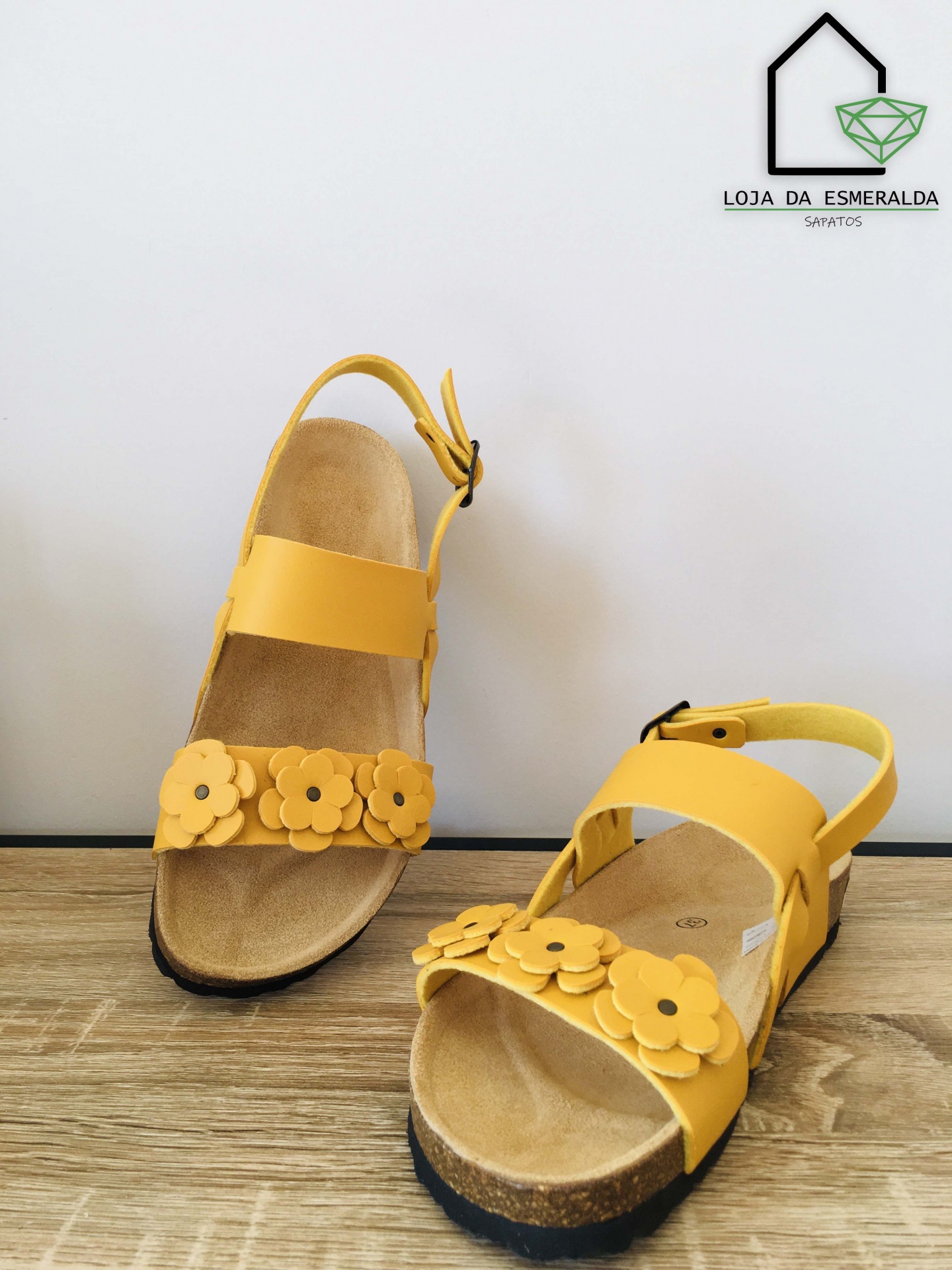 Sandálias amarelas com flores em couro e sola preta sobre madeira