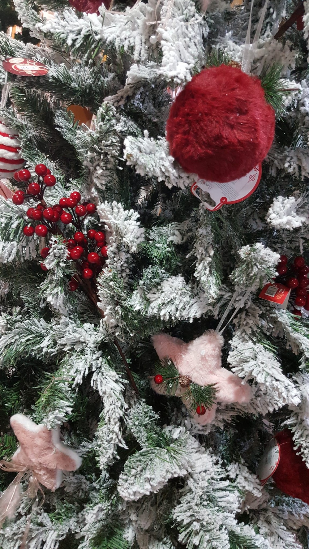 Árvore de Natal com decoração de neve artificial, bolas vermelhas peludas, estrelas cor-de-rosa e bagas vermelhas.