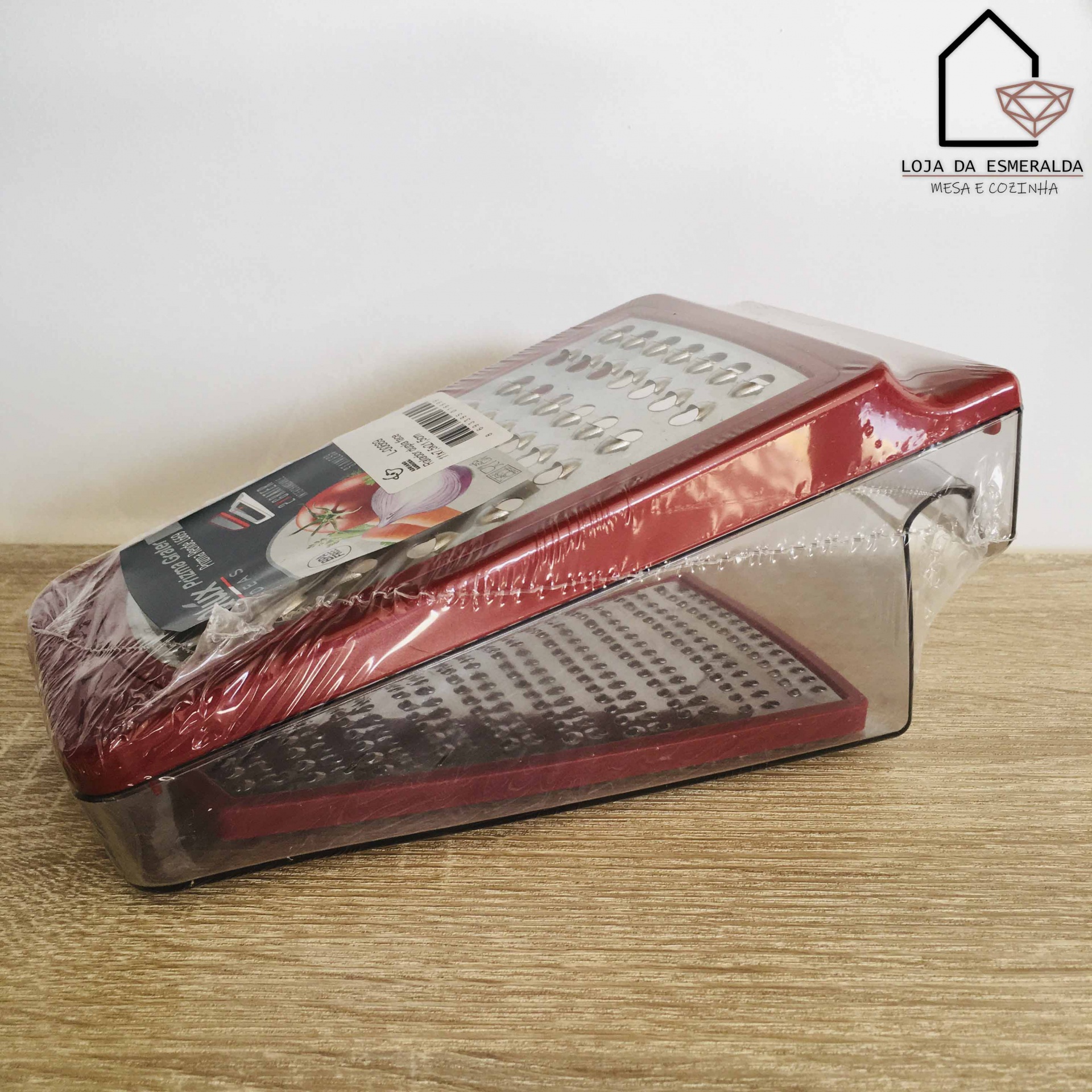 Ralador de cozinha com base plástica transparente e topo vermelho metálico sobre mesa de madeira.