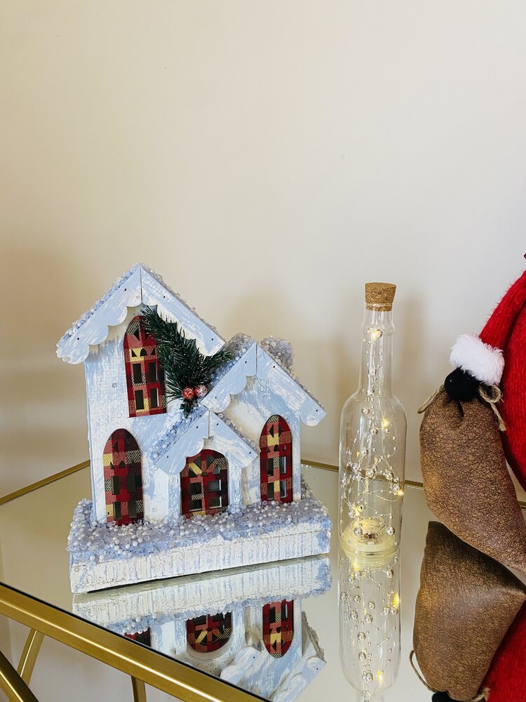 Casinha decorativa de natal com neve artificial e luzes numa garrafa ao lado