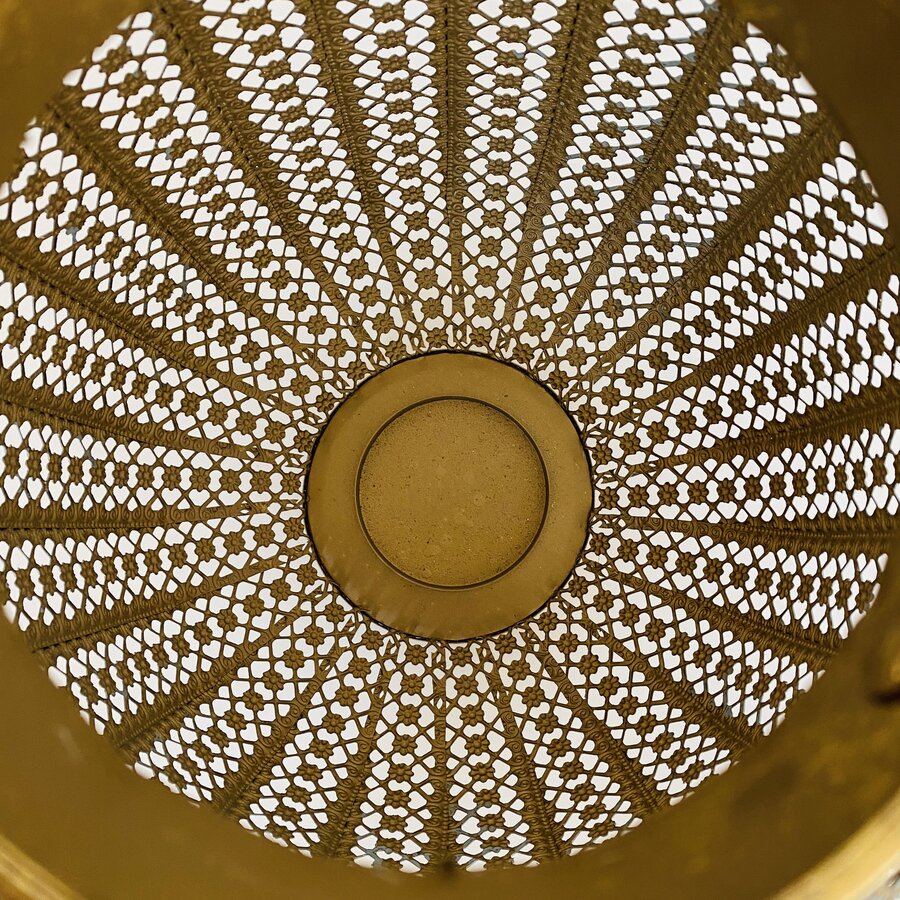 Interior de peneira metálica dourada com padrão perfurado hexagonal e radial.