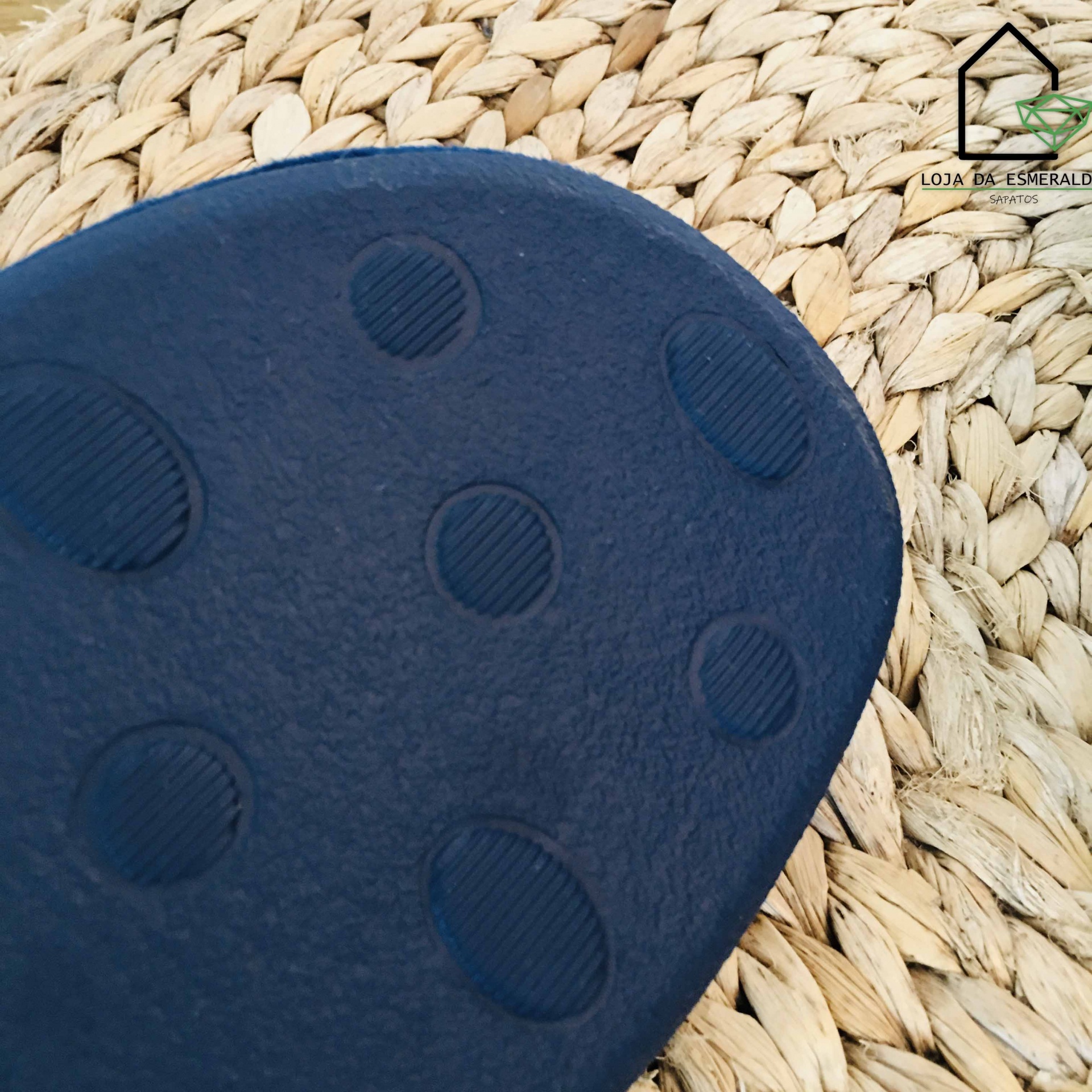 Sola azul escuro de chinelo com textura, sobre esteira de fibra e logo Loja das Esmeraldas no canto