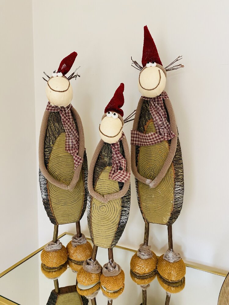 Três figuras decorativas de madeira com gorros vermelhos e cachecóis xadrez em superfície espelhada