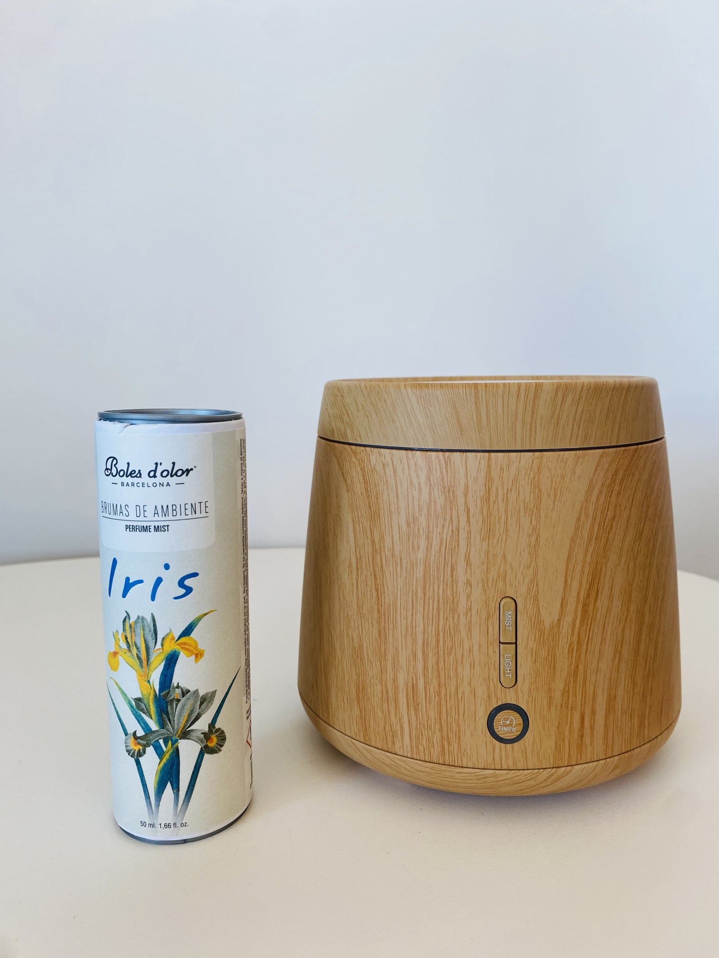 Difusor de ambiente em madeira clara ao lado de frasco cilíndrico de aromas com texto Iris e ilustração de flores