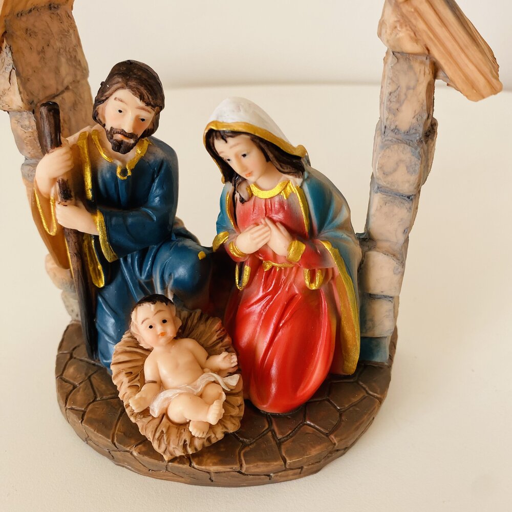 Miniatura de presépio com figuras de resina coloridas de José, Maria e Menino Jesus, base imitando pedra.