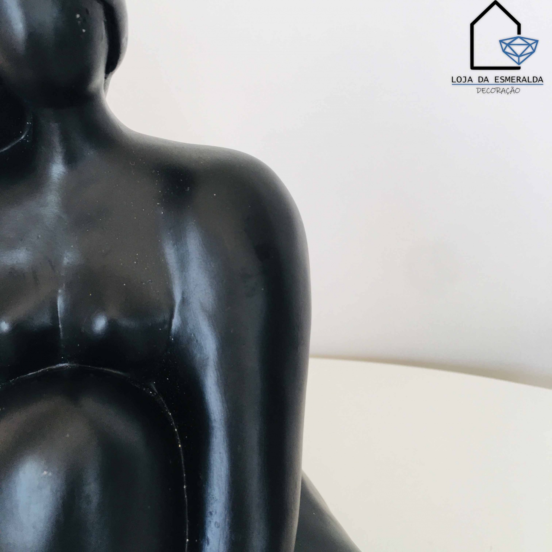 Escultura abstrata preta de corpo humano num ambiente branco com logótipo Loja da Esmeralda
