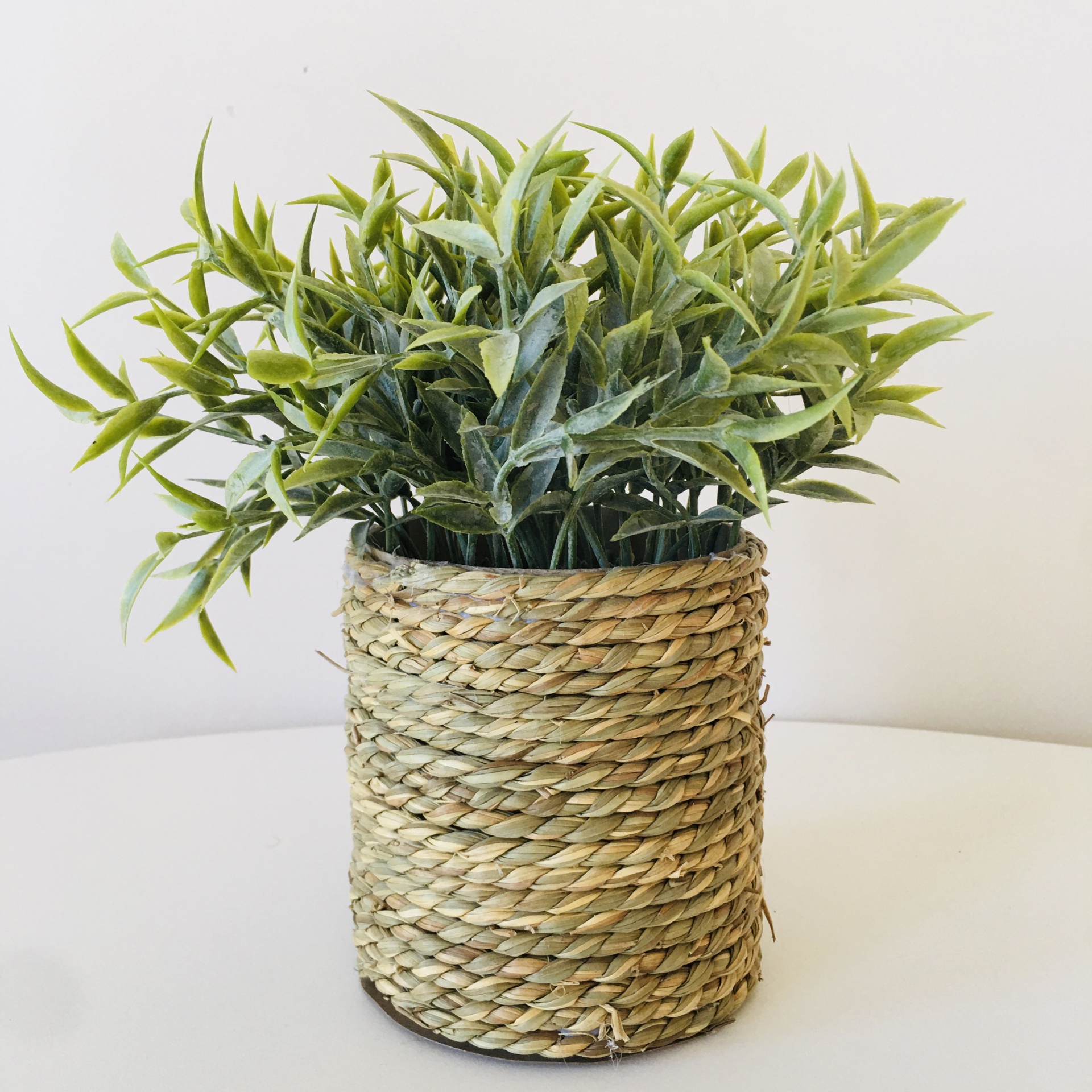 Planta artificial em vaso trançado natural sobre mesa branca